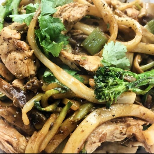 a plate of udon noodles with chicken, courgette and mushrooms